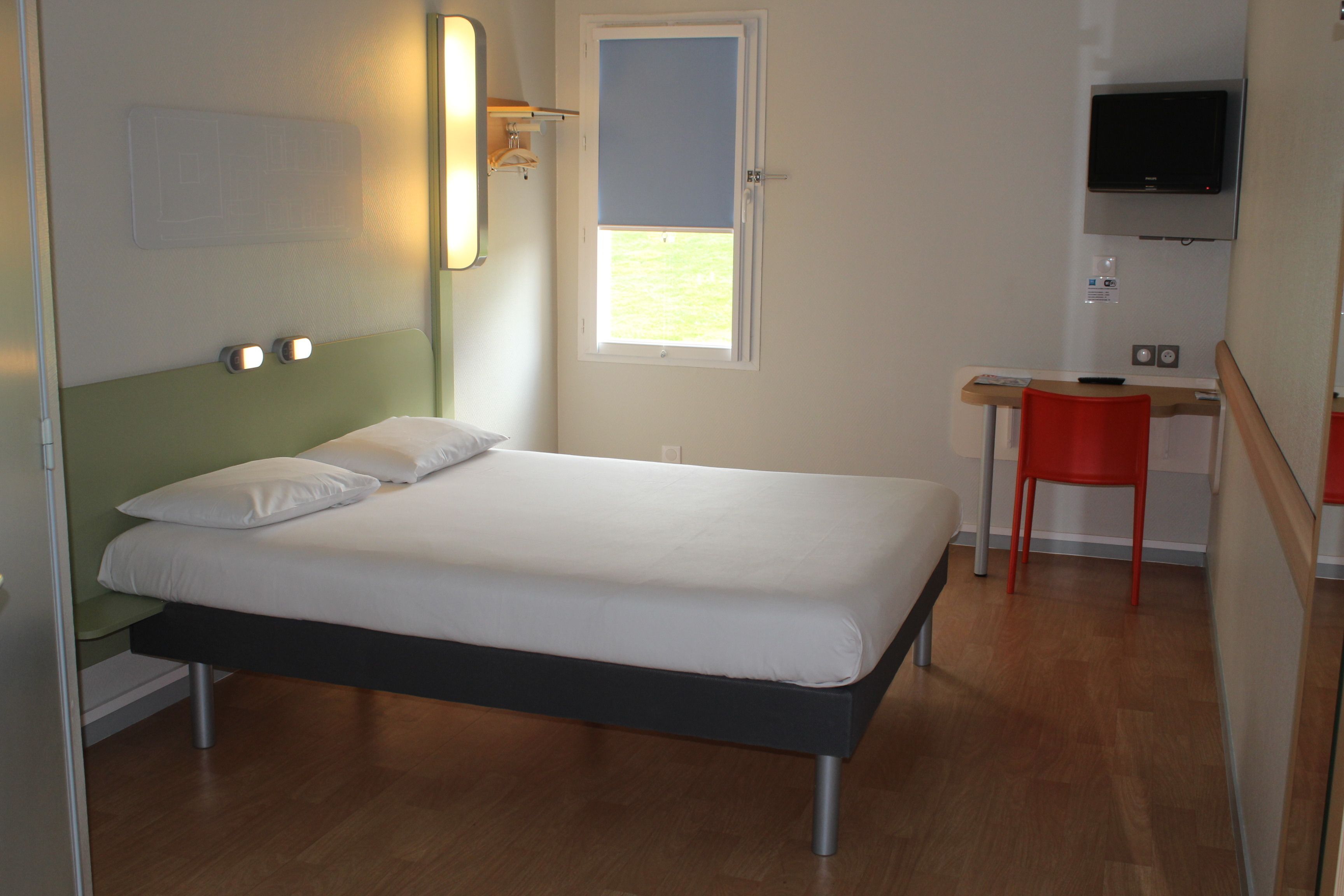 A room with a bed, a desk, a chair, and a TV.