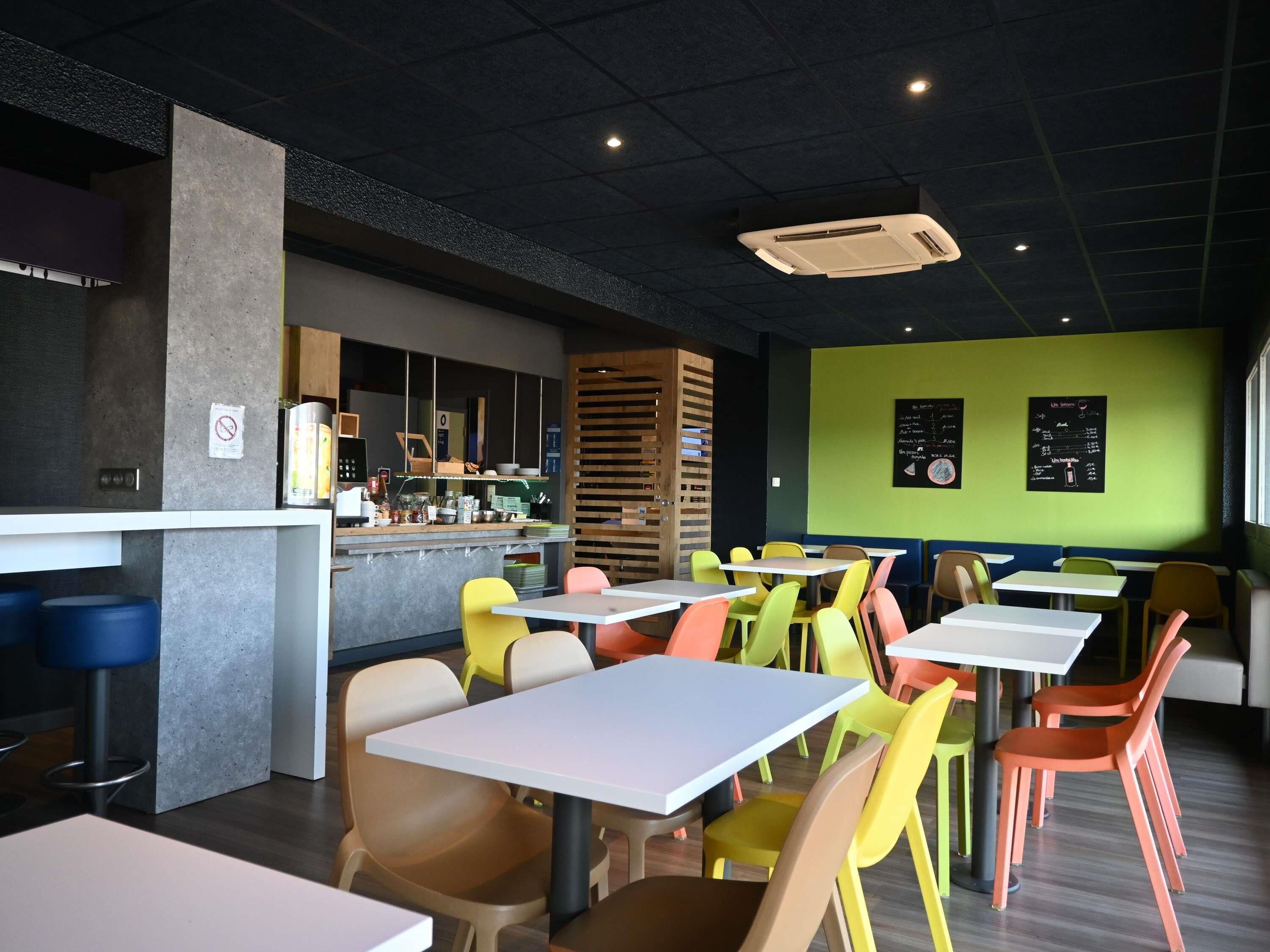 Interior modern d'un restaurant amb caires i taules de colors, i una barra amb un quadre de menú.