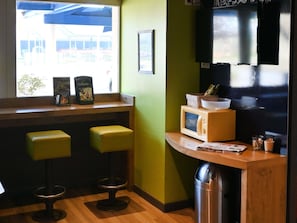 A small kitchenette with a microwave, a trash bin, and two stools. - ibis budget Laval (Bonchamp-les-Laval)