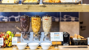 Un buffet de petit-déjeuner proposant divers types de céréales, des fruits et du pain.