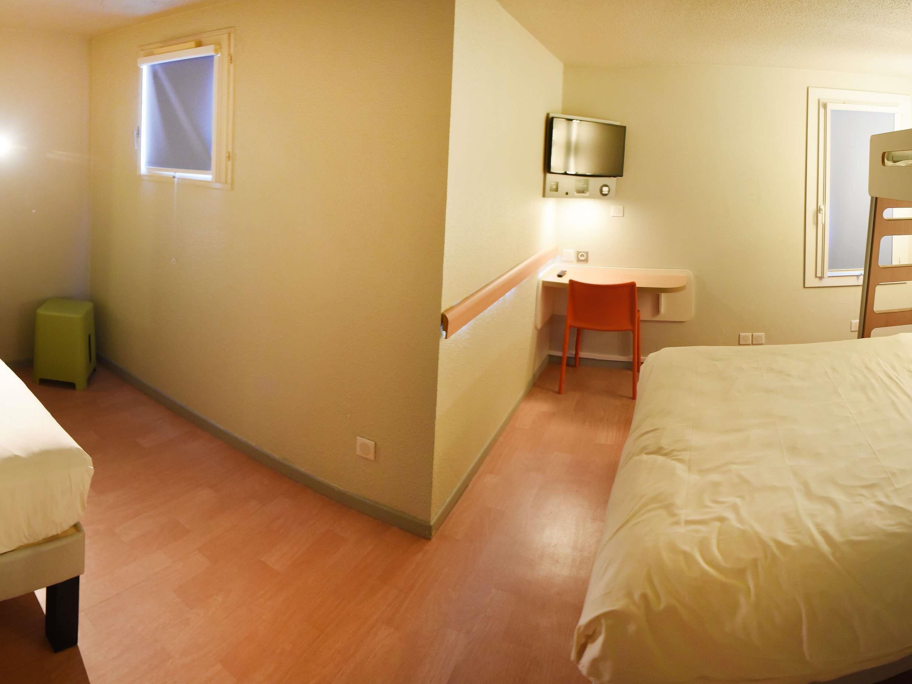 Une chambre d’hôtel avec un lit, un bureau, une chaise, une télévision et une fenêtre.
