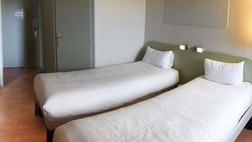 Ein Hotelzimmer mit zwei Einzelbetten, einer verschließbaren Tür und einer Wandleuchte.
