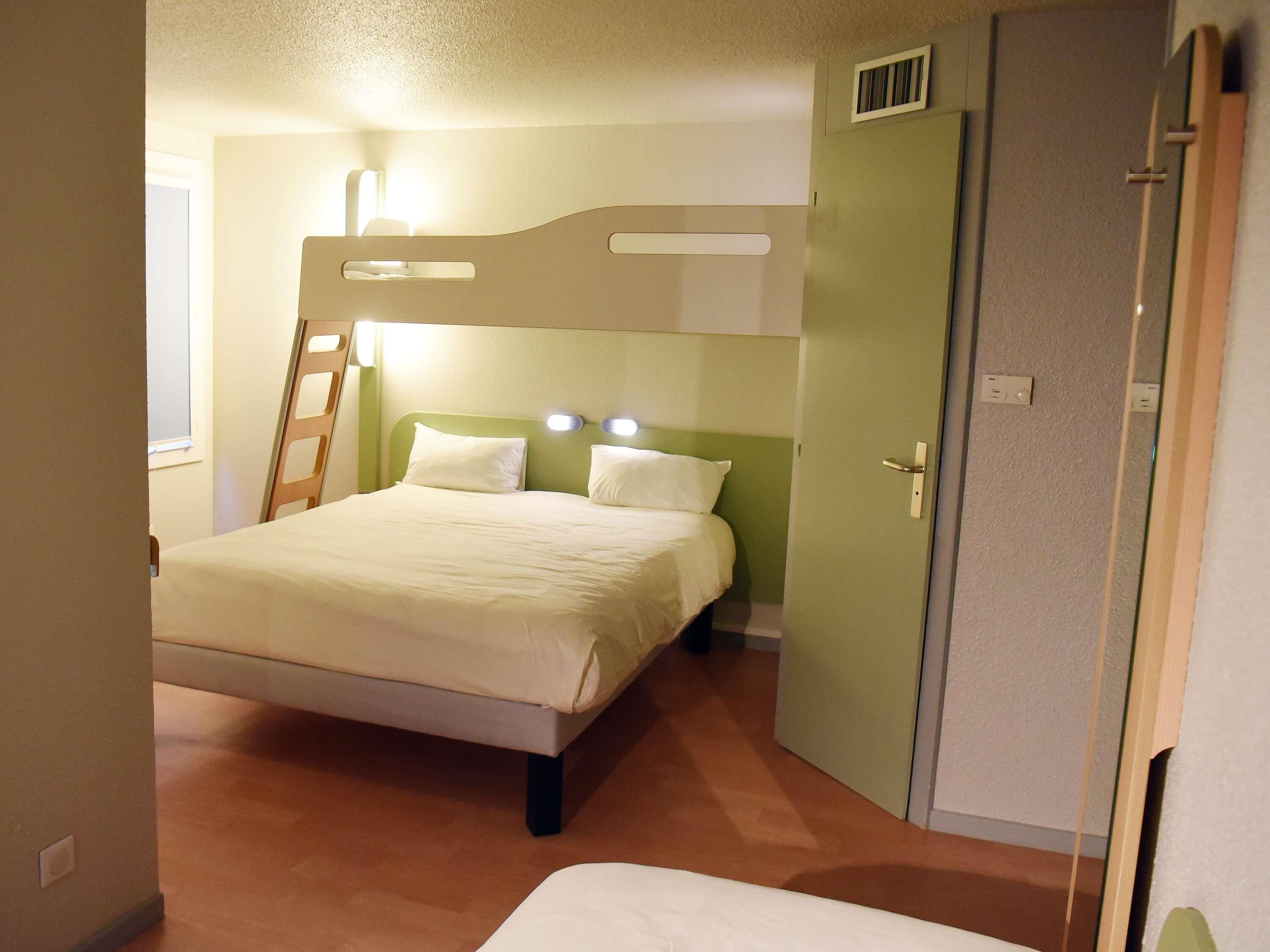 A single-bed room with a bunk bed, a ladder, a wardrobe, and a window.