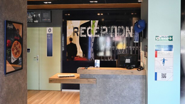 Un espace d’accueil doté d’un plancher en bois, d’un comptoir de réception et d’une enseigne fixée au mur sur laquelle on peut lire « RÉCEPTION ».