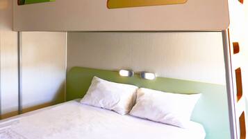 A hotel room with a bed, two pillows, a headboard with lights, and a green accent wall.