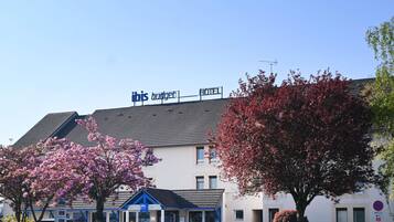 A hotel with a signboard, a parking area, and a tree with pink blossoms.