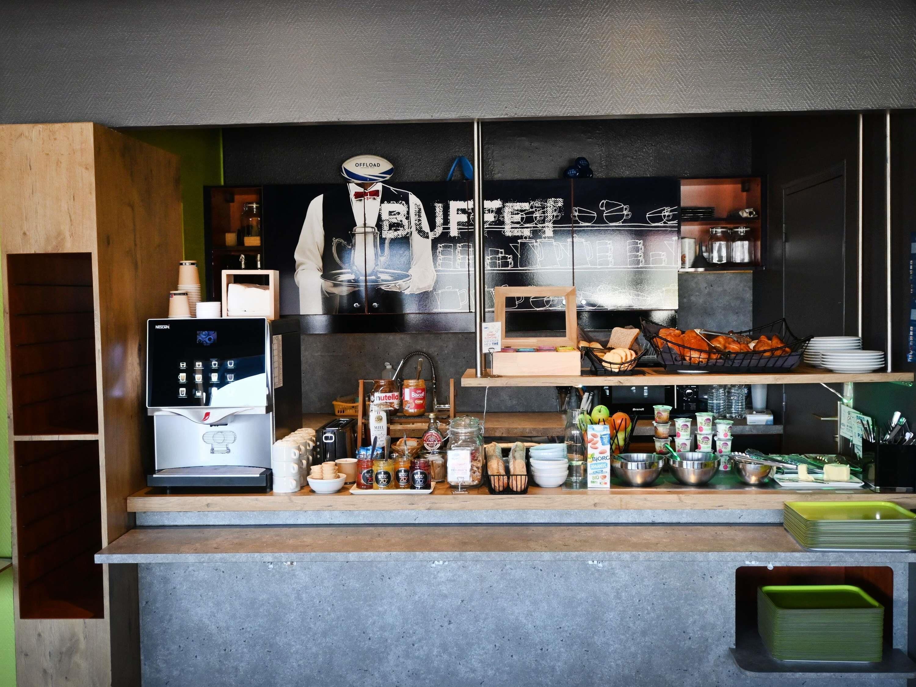 Un bancone di un bar con una macchina per il caffè, diversi cibi e una lavagna con il menu.