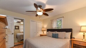 Un dormitorio con cama, ventilador de techo, mesita de noche, cómoda y ventana con cortinas.