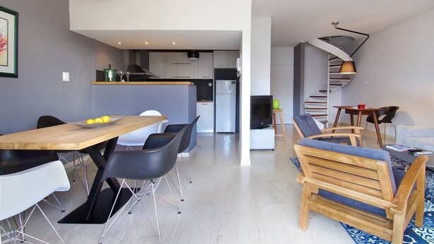 Une cuisine moderne avec un coin repas, un escalier et un salon comprenant un canapé et une table basse.