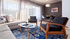Un salon moderne comprenant un canapé, deux fauteuils, une table basse et un coin repas agrémenté d’un lustre.