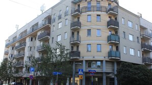 Een meerlaags appartementencomplex met balkons, een voetgangersoversteekplaatsbord en richtingaanduidingen.