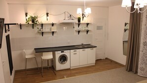 Een kleine keuken met een wasmachine, een spoelbak en een aanrecht met planken waarop planten en keukengerei staan.