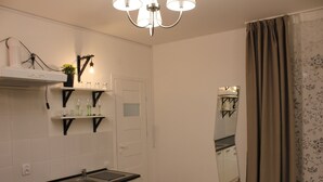 Een moderne keuken met witte kasten, een zwart aanrecht en een inbouwspoelbak. Daarboven hangt een kroonluchter en aan de muur een spiegel.