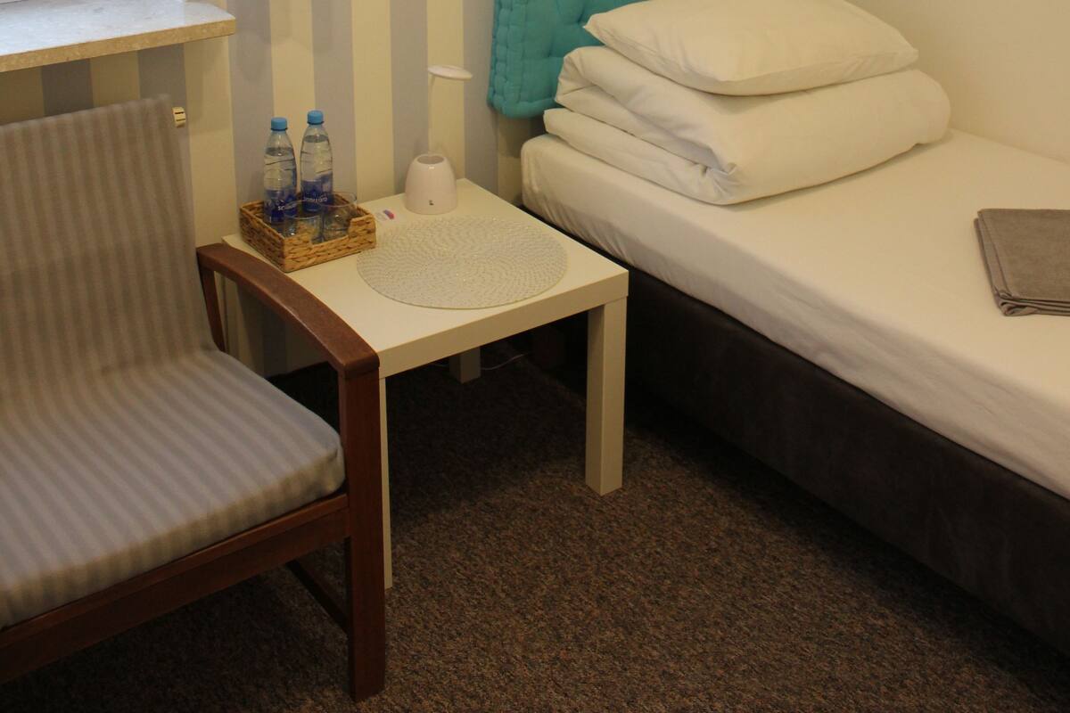 Une chambre d’hôtel avec un mur à rayures, un lit, une chaise, une petite table et une fenêtre avec des rideaux.