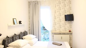 Een slaapkamer met een bed, een televisie aan de muur, een raam met gordijnen en een radiator.
