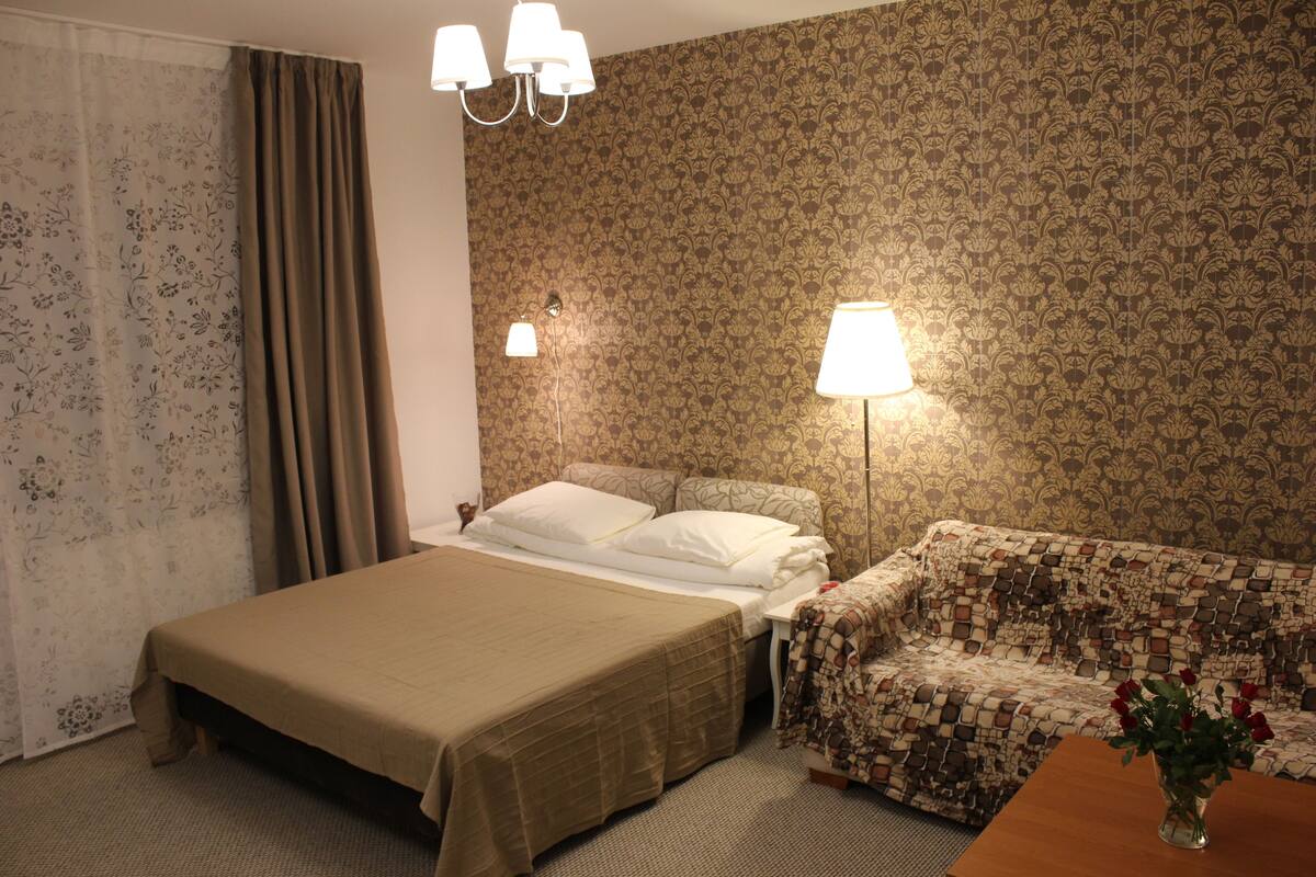Une chambre d’hôtel avec un lit, un canapé, une table de chevet avec des lampes et un rideau.
