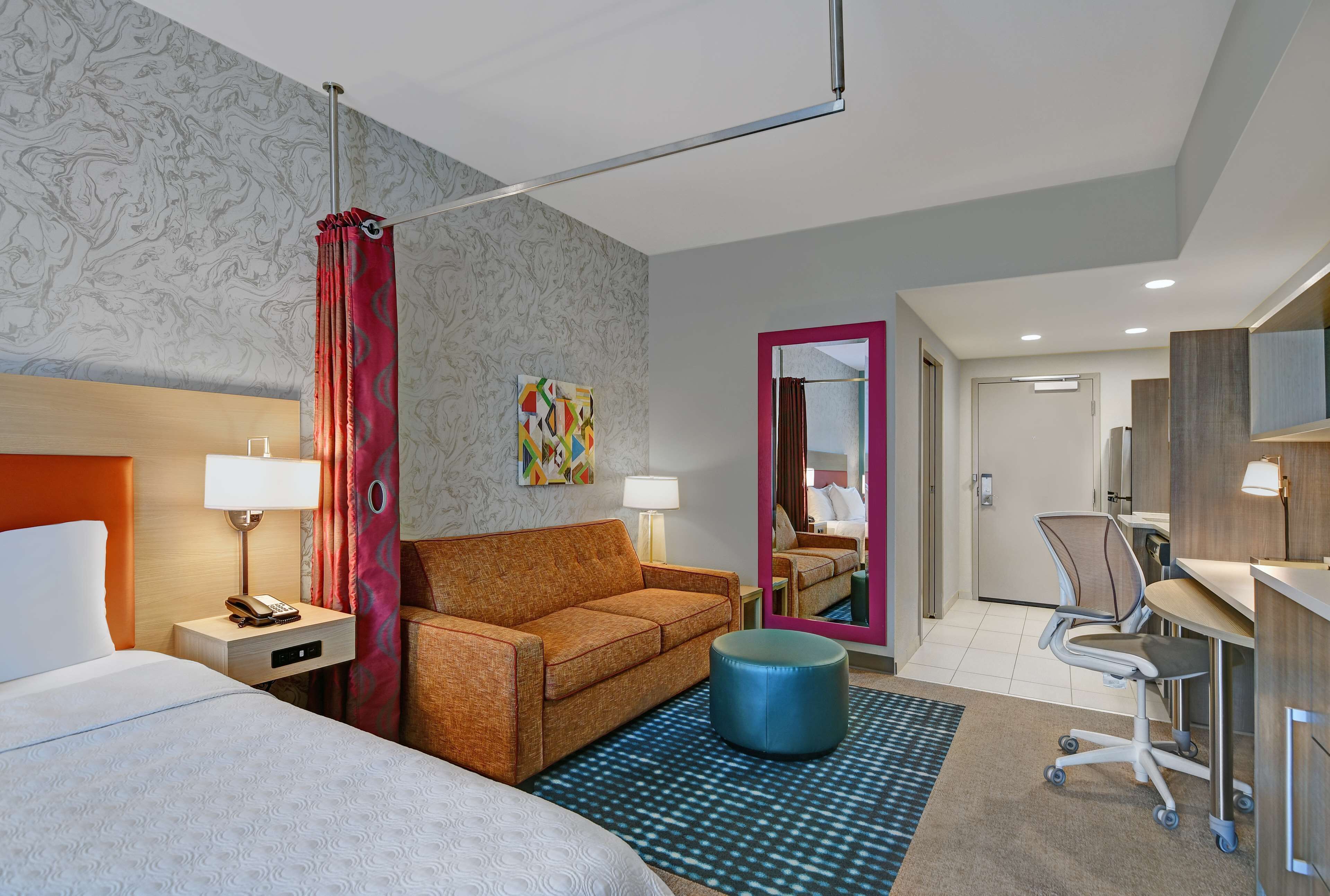 Habitación de hotel con cama, sofá, escritorio, silla, espejo y puerta de baño.