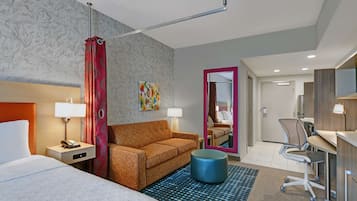 Habitación de hotel con cama, sofá, escritorio, silla, espejo y puerta de baño.