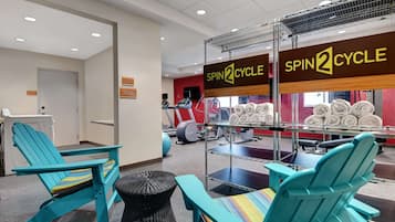Une salle de sport avec des chaises turquoise, un espace dédié au vélo d’appartement et du matériel d’exercice.