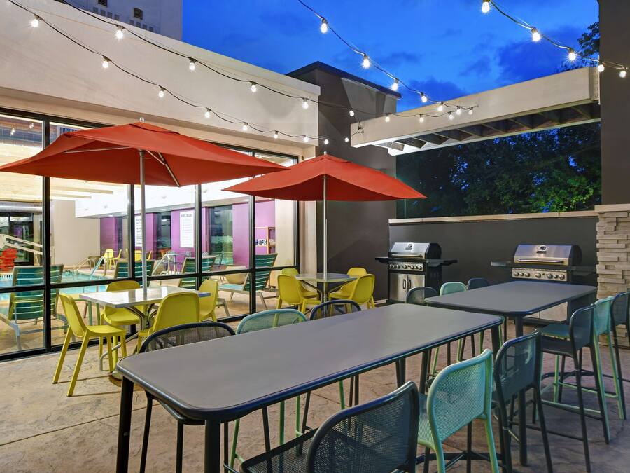 An outdoor dining area with tables and chairs, string lights, and a pool in the background.