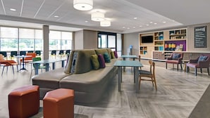 A modern lounge area with a sofa, chairs, tables, and a TV screen.