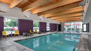 A swimming pool with clear water, surrounded by yellow and green chairs, and purple walls.