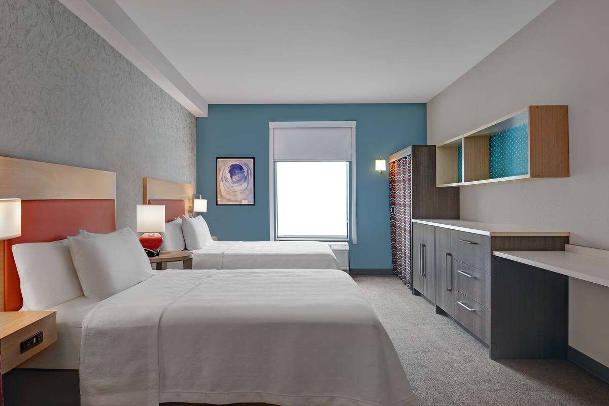 Ein Hotelzimmer mit zwei Betten, einem großen Fenster, einem Schreibtisch und einem Kleiderschrank.