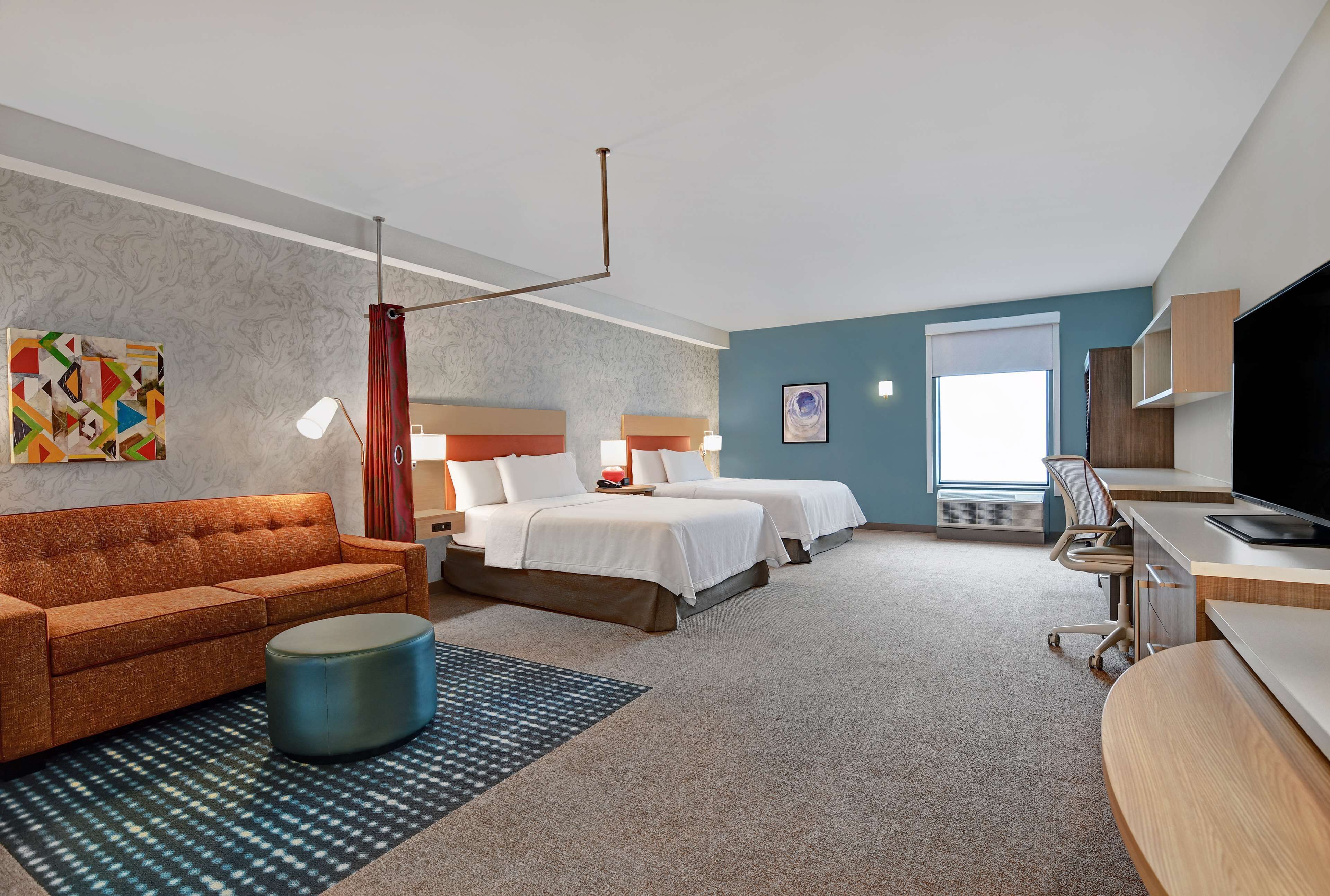 A hotel room with a sofa, two beds, a desk, and a TV.