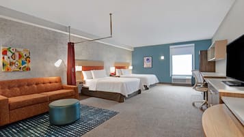 A hotel room with a sofa, two beds, a desk, and a TV.