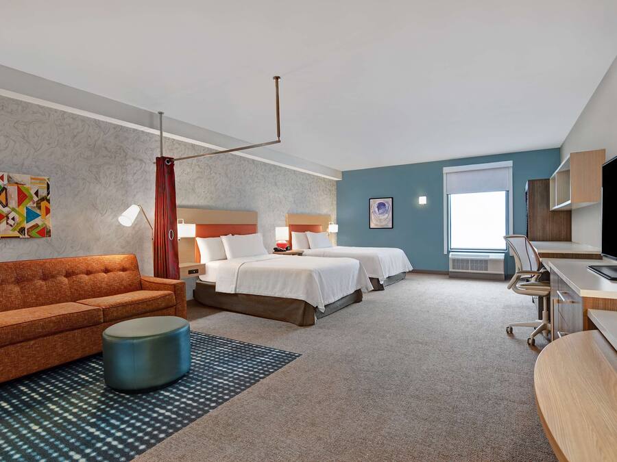 A hotel room with a sofa, two beds, a desk, and a TV.