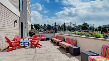 Une terrasse extérieure avec des fauteuils Adirondack rouges, une table bleue et des canapés à rayures.