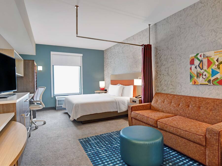 Een hotelkamer met een bed, een bureau met een televisie, een bank, een stoel, een lamp en een schilderij aan de muur.