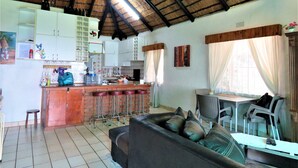 A kitchen with a bar area, a dining table with chairs, a sofa, and a TV. - Viewpoint Lodge (Mbombela)