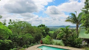 A rectangular pool with a clear blue water surface, surrounded by lush greenery and a view of distant hills. - Viewpoint Lodge (Mbombela)