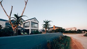 Una casa moderna con un amplio frente de vidrio, rodeada de vegetación exuberante y un camino de tierra.