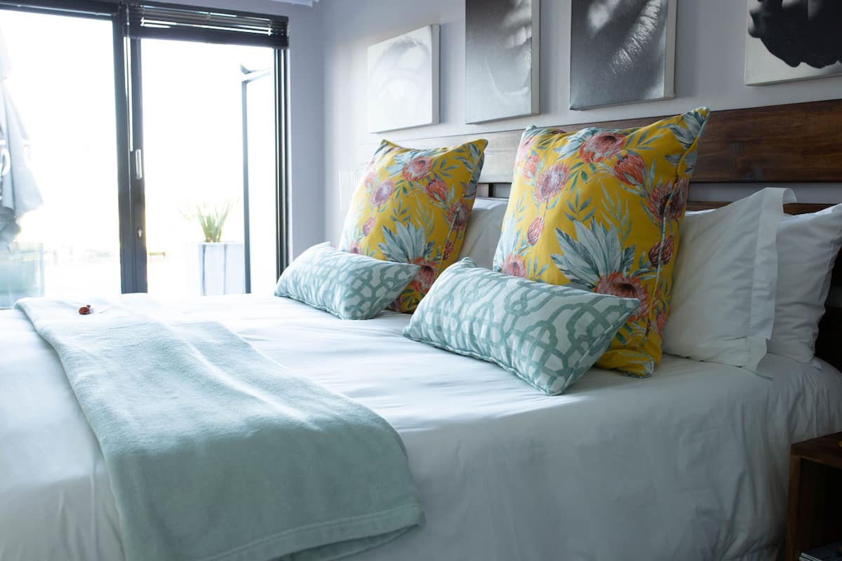 A bed with white bedding, two floral pillows, and a light blue throw blanket.