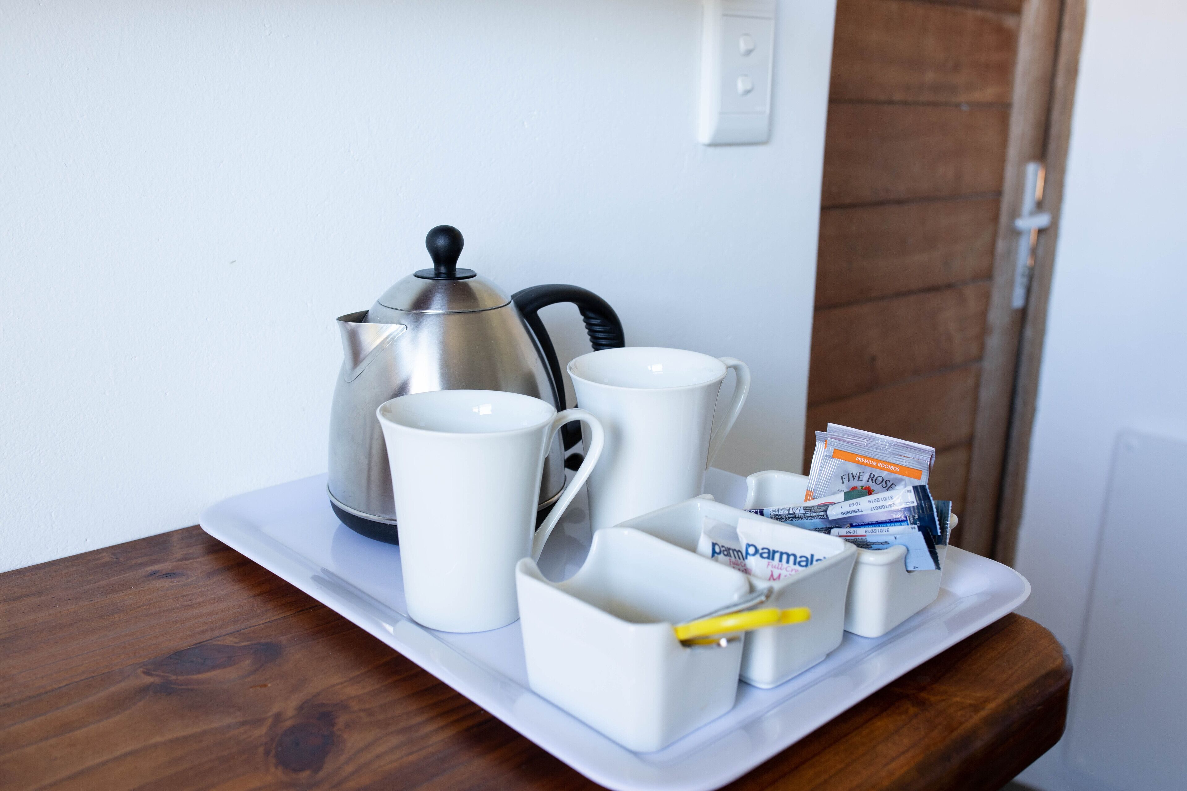 A tray with a silver coffee pot, two white mugs, a white cup, and a small white container with a yellow pen.