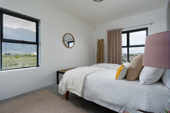 Un dormitorio con cama, ventana, espejo y vistas al exterior.