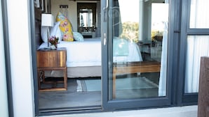Un dormitorio con cama, mesita de noche, lámpara y vistas a través de un ventanal.
