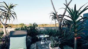 Un patio con una silla de descanso, una mesa con un cuenco y vasos, y diversas plantas.