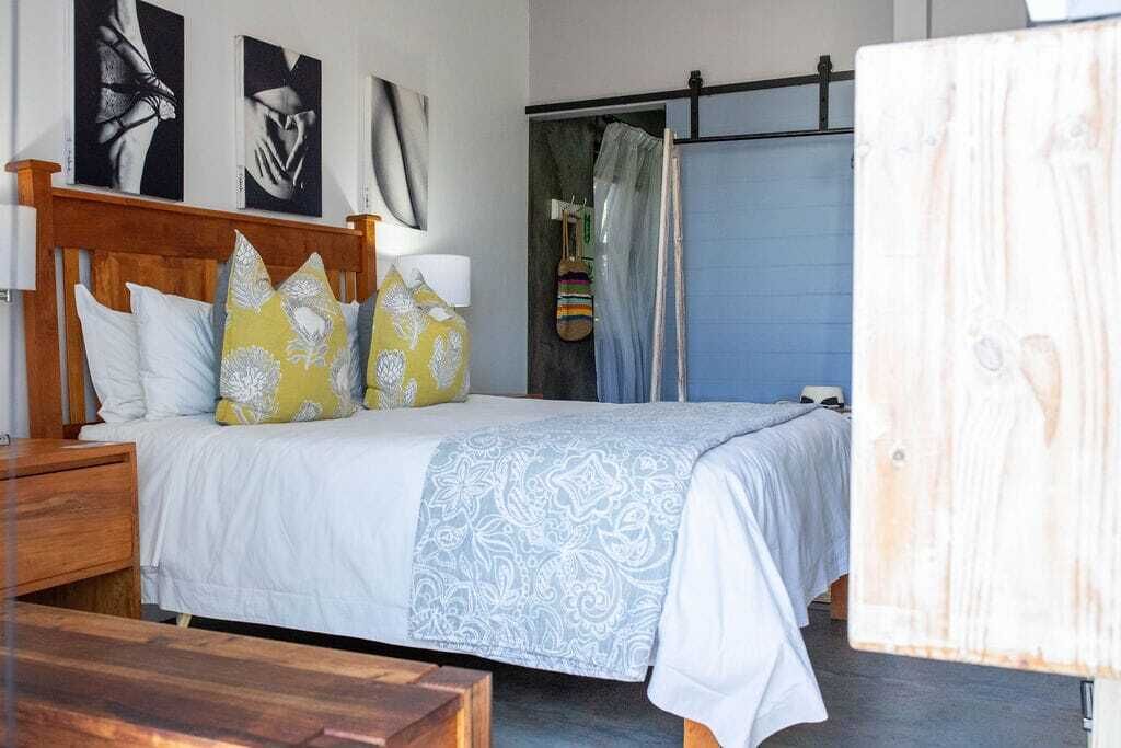 A bed with a wooden headboard, multiple pillows, a patterned blanket, and a bedside table.