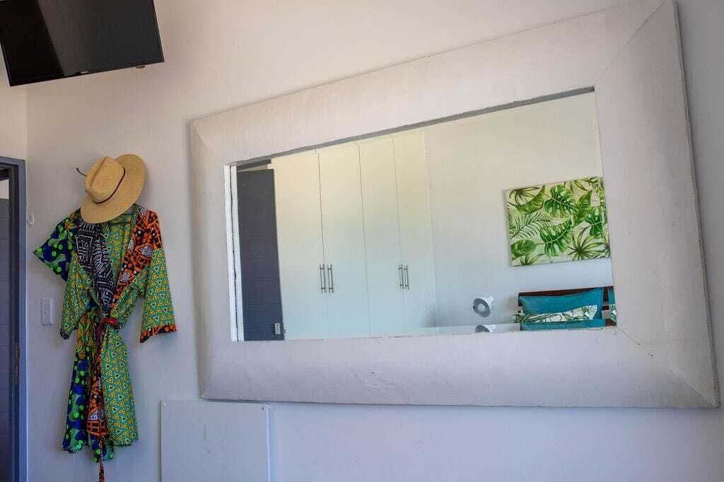 Un baño con un espejo grande, un perchero con un sombrero y una toalla verde estampada.
