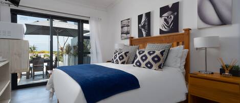 Un dormitorio con cama, mesita de noche, escritorio y puerta corrediza de vidrio que da a un espacio exterior.