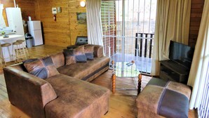 L’intérieur chaleureux d’un chalet comprend un espace de vie avec un canapé, un téléviseur et un coin repas équipé d’un réfrigérateur et de tabourets de bar.