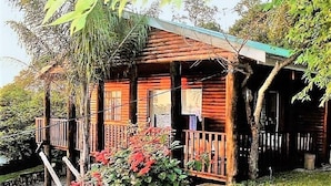 Une cabane en bois dotée d’un porche, entourée d’une végétation luxuriante et d’un petit étang.