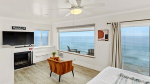 Une chambre d’hôtel dotée d’une grande fenêtre donnant sur l’océan, d’une télévision, d’une cheminée et d’un coin salon confortable.