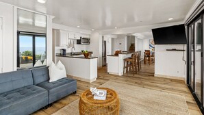 Un salon moderne comprenant un canapé, un coin repas, une cuisine avec un grand îlot central et un téléviseur fixé au mur.