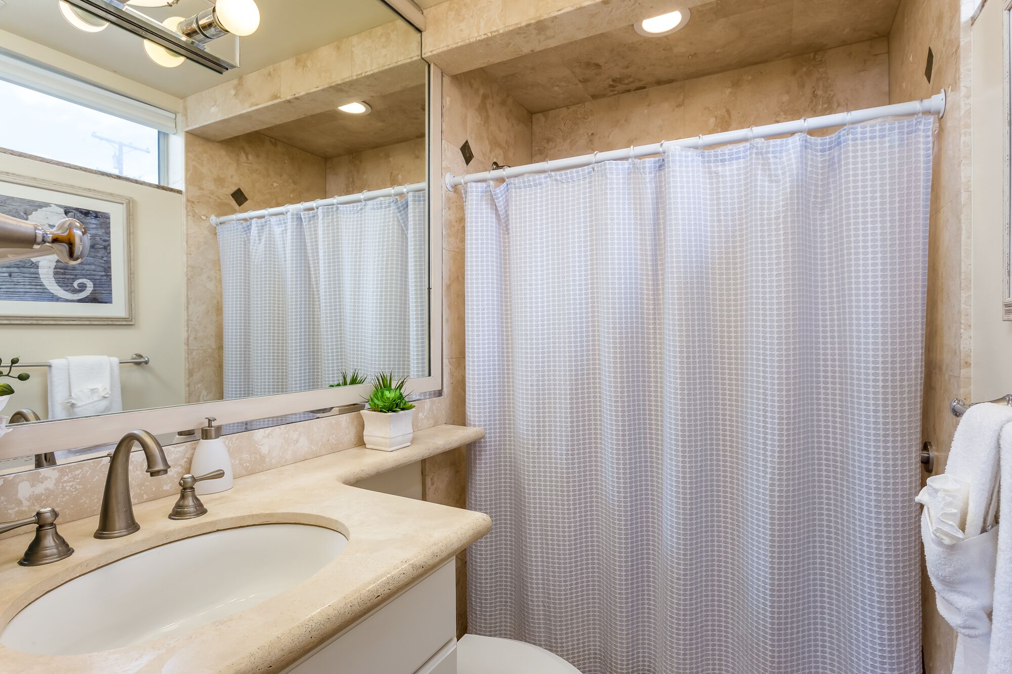 A bathroom with a large sink, a mirror, a shower curtain, and a towel rack.