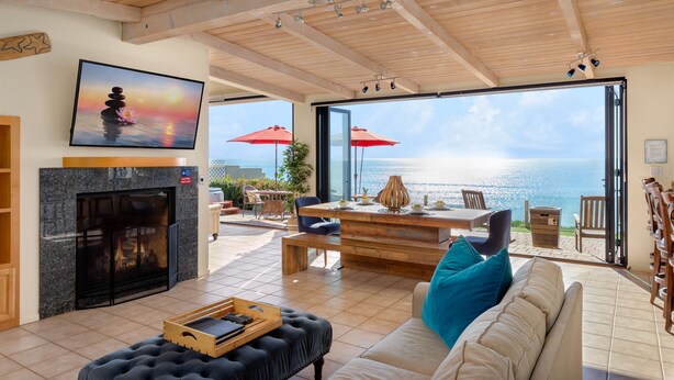 A spacious living room with a fireplace, a large TV, and a view of the ocean through open doors. - Seaside Luxury Duplex with Putting Green E950-0 (Encinitas)