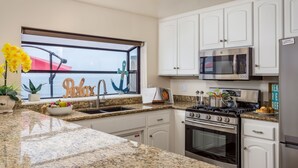A kitchen with white cabinets, a granite countertop, a stove, a microwave, and a refrigerator. - Seaside Luxury Duplex with Putting Green E950-0 (Encinitas)